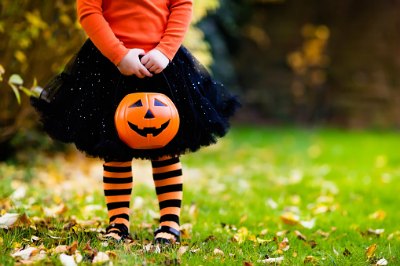 little girl in orange top and black skirt holding a halloween pumpkin bucket